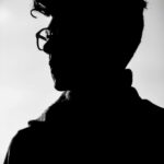 Artistic black and white profile silhouette of a man wearing eyeglasses.